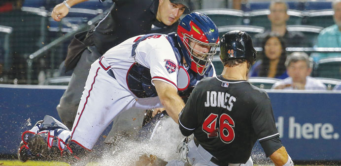 Atlanta Braves catcher Evan Gattis (centre) tags out Miami Marlins first baseman Garrett Jones (right) as home plate umpire Eric Cooper watches the pl