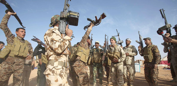 Fighters from a Shia paramilitary group hold up their weapons near the village of Nukhayb in Anbar province yesterday.