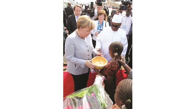 German Chancellor Angela Merkel receives a calebasse of water from a girl as Malian President Ibrahim Boubacar Keita looks on at Bamako airport yesterday.