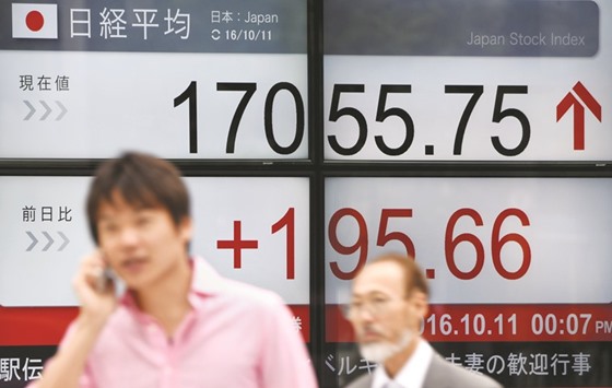 People walk past an electronic quotation board flashing the Nikkei key index in front of a securities company in Tokyo. Japanese shares rose yesterday, extending a global rally, as a jump in oil prices boosted energy firms while exporters won support from a weaker yen.