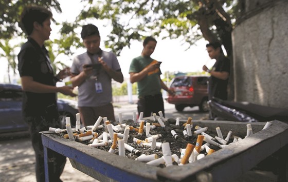 Men smoke cigarettes near a tray filled with stubs beside a road in Las Pinas city, Metro Manila.