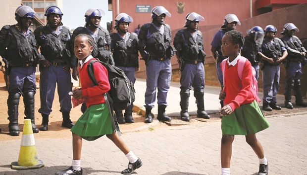School girls walk past riot police standing guard outside Hillbrow magistrate court during an appearance of students who were arrested during a protest demanding free education at the Johannesburgu2019s University of the Witwatersrand.