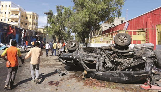 People walk past the wreckage of a car at the scene of an attack on a restaurant by the Somali extremist group Shebaab in Mogadishu.