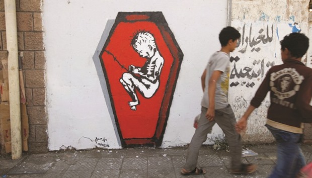 Boys walks pass a graffiti of artist Murad Subai, depicting a child suffering from malnutrition in a coffin, along a street in Sanaa. The graffiti is part of a campaign by several artists titled u2018Ruinsu2019 which focuses on the issue of malnutrition, hunger and disease because of war.