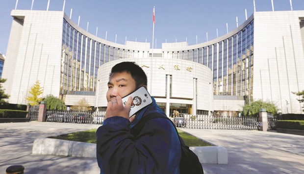 A man uses his mobile phone while walking past the headquarters of the Peopleu2019s Bank of China in Beijing. PBoC officials met with commercial banks and urged them to move away from a dependence on borrowing via overnight bond repurchase agreements, the most common form of short-term interbank lending in China.