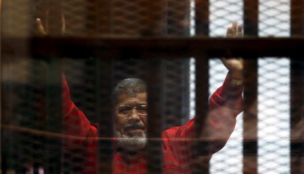 Egypt's deposed president Mohamed Mursi greets his lawyers and people from behind bars at a court wearing the red uniform of a prisoner sentenced to death, during his court appearance with Muslim Brotherhood members on the outskirts of Cairo, Egypt.  June 21, 2015 file picture.