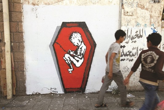 Boys walks pass a graffiti of artist Murad Subai depicting a child suffering from malnutrition in a coffin along a street in Sanaa, Yemen. The graffiti is part of a campaign by several artists titled u201cRuinsu201d which focuses on the issue of malnutrition, hunger and disease because of war.