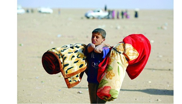 An Iraqi refugee boy who fled Mosul carries blankets following his arrival in the desert area of Rajam al-Saliba on the Iraq-Syria border south of Al-Hol in Syriau2019s Hassakeh province.