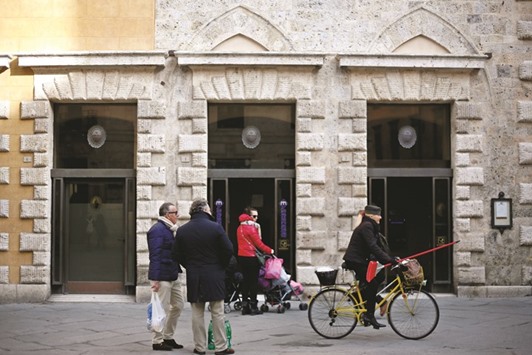 Pedestrians pass a Banca Monte dei Paschi di Siena branch in Siena, Italy. Its shares lost nearly 15% at close after the troubled lender unveiled plans to axe 2,600 jobs and close 500 branches.