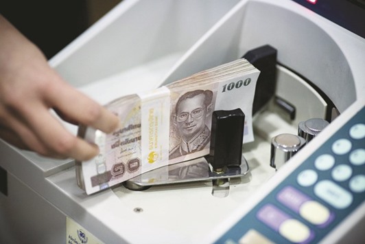 An employee places a bundle of baht banknotes in a money counting machine in an arranged photograph at the Krung Thai Bank headquarters branch in Bangkok. The baht weakened 0.1% to 34.977 per dollar yesterday.