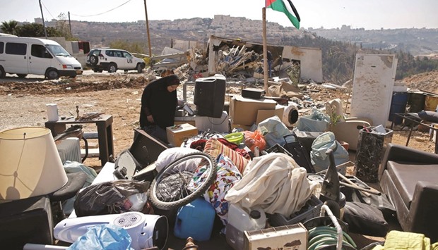A Palestinian woman searches through her belongings after her family home was demolished by workers from the Jerusalem municipality in the mostly Arab East Jerusalem neighbourhood of Beit Hanina, near the Israeli settlement of Ramat Shlomo (background), yesterday. Palestinian homes built without an Israeli construction permit are often demolished by order of the Jerusalem municipality.