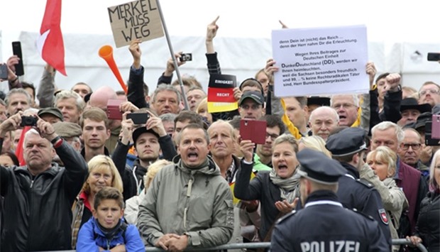 Police watches protestors holding a placard ,Merkel must go,