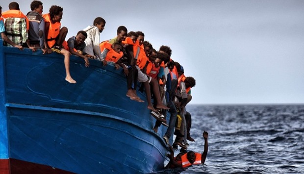 Migrants hang from a boat as they wait to be rescued as they drift in the Mediterranean Sea some 20 nautical miles north off the coast of Libya.
