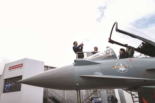 An attendee takes a photograph of a friend sitting in a Eurofighter Typhoon fighter jet, manufactured by BAE Systems, on the second day of the International Airshow 2016 in Farnborough, UK. At least 10% of posts at London-based BAEu2019s military-aircraft unit will go, mostly in northwest England, together with hundreds of positions at the maritime division and up to 150 at the cyber arm, the company said yesterday.