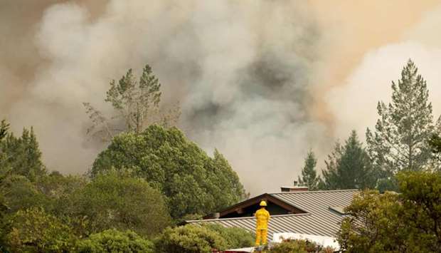 A firefighter watches smoke billow as flames approach a residential area in Sonoma in California