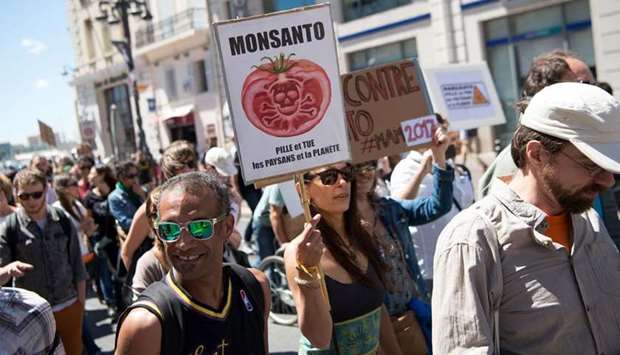 Demonstrators walk with a placard reading 'Monsanto robs and kills farmers and our planet'