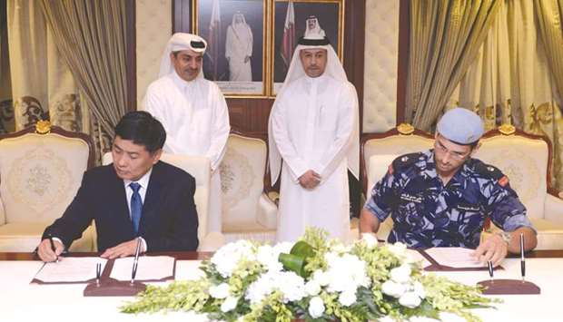 HE Dr Issa Saad al-Jafali al-Nuaimi looks on as Major Ali Hassan al-Rashed and Wang Weidong sign an agreement in Doha yesterday.