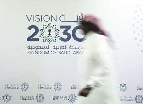 A Saudi man walks past the logo of the Vision 2030 after a news conference in Jeddah (file). The analysts in the Reuters poll have become significantly more gloomy about Saudi growth than the IMF, which expects the economy to expand 0.1% this year.