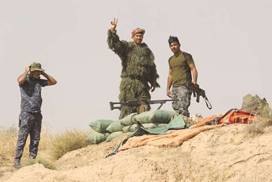 Iraqi forces gesture from a river bank across from Kurdish peshmerga positions yesterday, on the southern outskirts of Kirkuk.