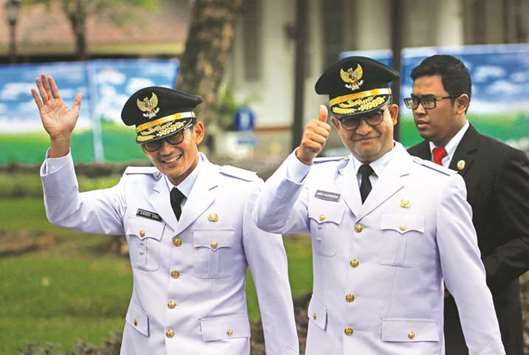 Jakarta Governor Anies Baswedan (right) and his deputy Sandiaga Uno wave to reporters before a swearing-in at the Presidential Palace in Jakarta.
