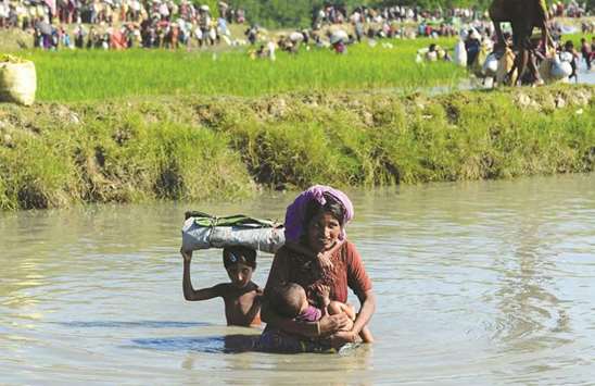 A Rohingya woman carries a child as they cross a shallow canal after crossing the Naf River as they flee violence in Myanmar to reach Bangladesh in Palongkhali near Ukhia.