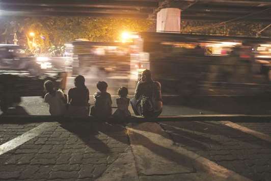 Passengers sit on the sidewalk as jeepneys pass them in Manila yesterday.