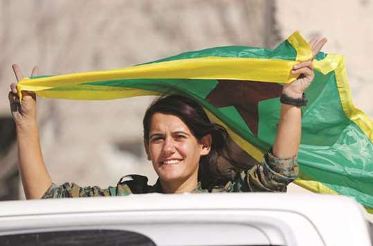 A female fighter of Syrian Democratic Forces waves a flag while riding on a pick up truck in Raqa.
