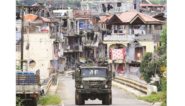Soldiers on a military truck drive past houses and buildings damaged after government troops cleared the area from pro-Islamic State militant groups inside the war-torn Marawi city, southern Philippines.