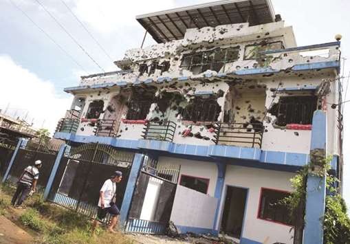 People walk in front of a bullet-riddled apartment house in a residential area in Malutlut district, Marawi city, southern Philippines  yesterday, which was believed to have been rented by pro-Islamic State militant group leaders before their battle in Marawi city.