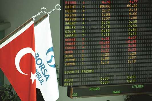 The Turkish national flag (left) and the Borsa Istanbul flag hang alongside financial data displayed on electronic boards inside the Borsa Istanbul in Istanbul (file). Turkey is among the 10 best-performing markets this year, with the Istanbul gauge advancing 34%.