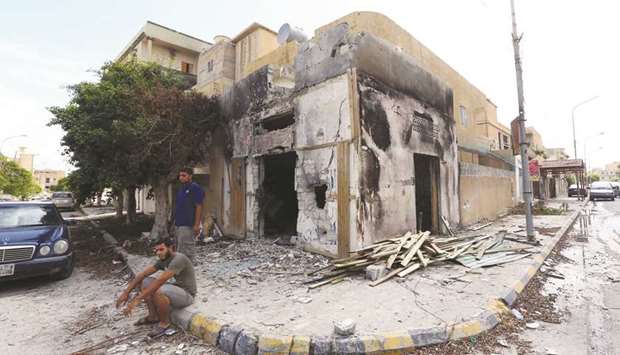 Libyans sit next to a damaged house in Sabratha yesterday, after three weeks of deadly fighting.