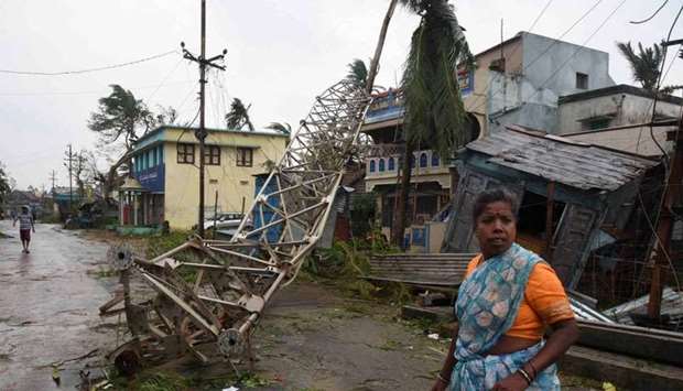 A woman stands next to a damaged communication tower after cyclone Titli hit in Srikakulam district