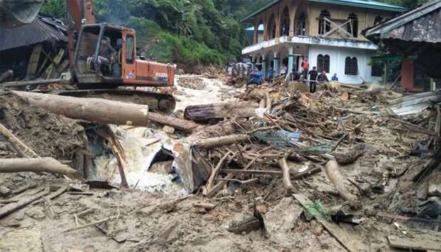 People use a heavy equipment to remove debris after flash floods hit the Saladi village in Mandailing Natal