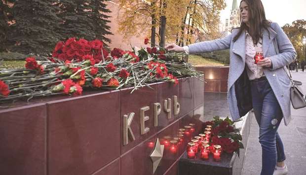 A woman lights a candle and lays flowers at the WWII Hero Cities Memorial to the city of Kerch after nineteen people were killed and dozens more wounded after a student opened fire today in a technical college in the Russian-annexed Crimean city.
