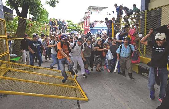 Honduran migrants, heading in a caravan to the US, rush through the Guatemala-Mexico international border bridge after tearing down its gate in Ciudad Hidalgo, Chiapas state, Mexico.