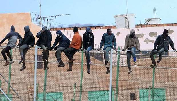 Migrants sit atop a border fence separating Morocco from the north African Spanish enclave of Melilla