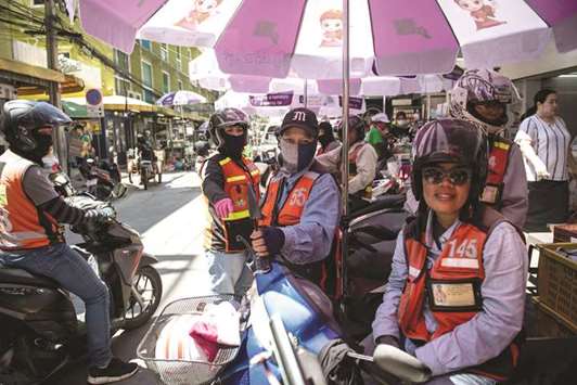 Three female motorcycle-taxi drivers waiting at a motorcycle-taxi stand in Bangkok.