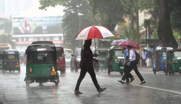 Pedestrians cross a street while sheltering under an umbrella during a heavy downpour in Colombo yesterday.