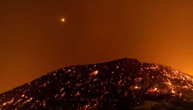 The moon shines through the smoke over a hillside of embers of the Saddleridge Fire in the Porter Ranch section of Los Angeles, California in the early morning hours