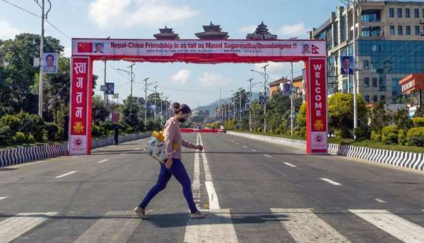 A woman crosses a road in front of a banner welcoming China's president Xi Jinping ahead of his state visit, in Kathmandu