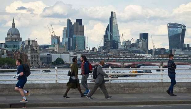 The skyline of buildings in The City of London is seen from Waterloo Bridge as pedestrians walk by in central London