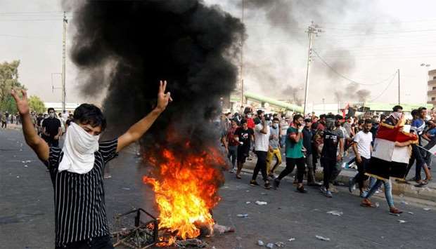 A demonstrator gestures as he stands close to burning tires blocking a road, during a protest over unemployment, corruption and poor public services, in Baghdad