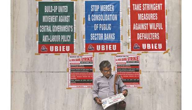A bank employee reads a newspaper in front of a United Bank of India branch building during a day-long strike against mergers of several state-run banks, in Kolkata, yesterday.