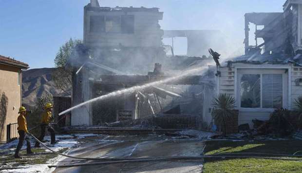 Firefighters hose down a burning house during the Tick Fire in Agua Dulce near Santa Clarita, California