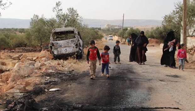 Syrians walk past a damaged van at the site of helicopter gunfire which reportedly killed nine people near the northwestern Syrian village of Barisha in the Idlib province along the border with Turkey, where ,groups linked to the Islamic State (IS) group, were present, according to a Britain-based war monitor with sources inside Syria.