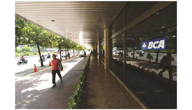 A pedestrian walks past by Bank Central Asia logo in Jakarta. BCA has the lowest operating-expense ratio of Indonesiau2019s biggest traded banks, data compiled by Bloomberg show.