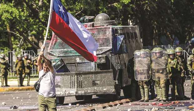 A demonstrator holding the Chilean national flag walks in front of a police vehicle during a protest in Santiago.