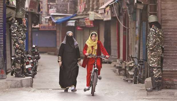 A Kashmir girl rides her cycle past security force personnel standing guard in front of closed shops in a street in Srinagar, yesterday.
