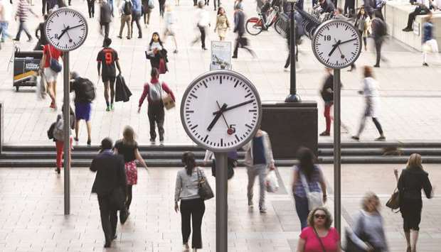 Pedestrians walk past clocks in the Canary Wharf financial, shopping and business district in London.