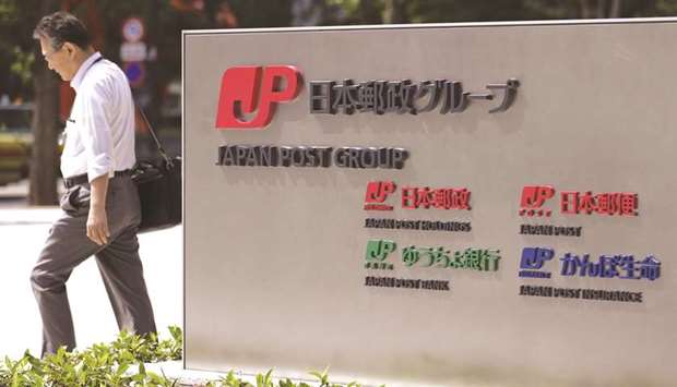 A pedestrian walks past signage for Japan Post Group in Tokyo.